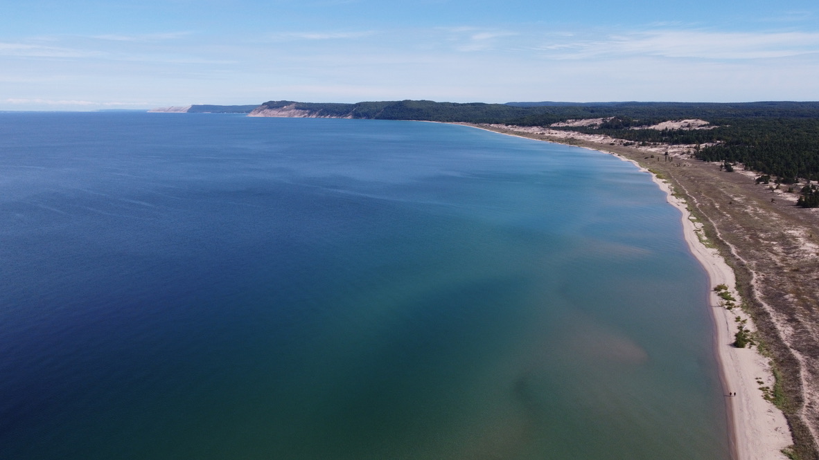 A sweeping blue bay bordered by a long sandy beach, dunes, and forest, photographed from my drone.